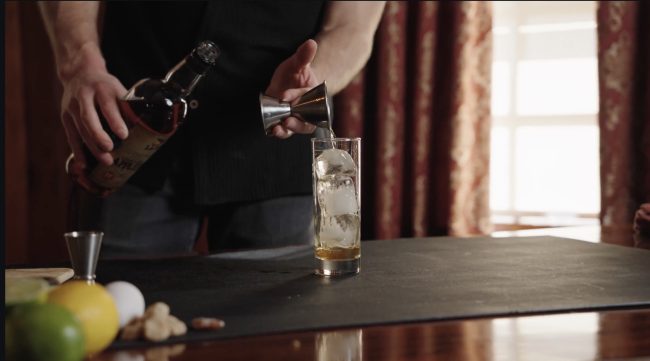 A highball glass filled with Laird's Apple Snap cocktail, garnished with a lemon wheel and ginger candy.